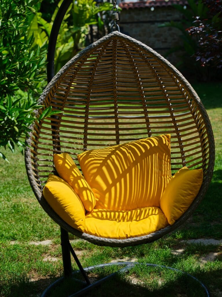 Relax in a stylish hanging egg chair with bright yellow cushions, set in a tranquil garden.